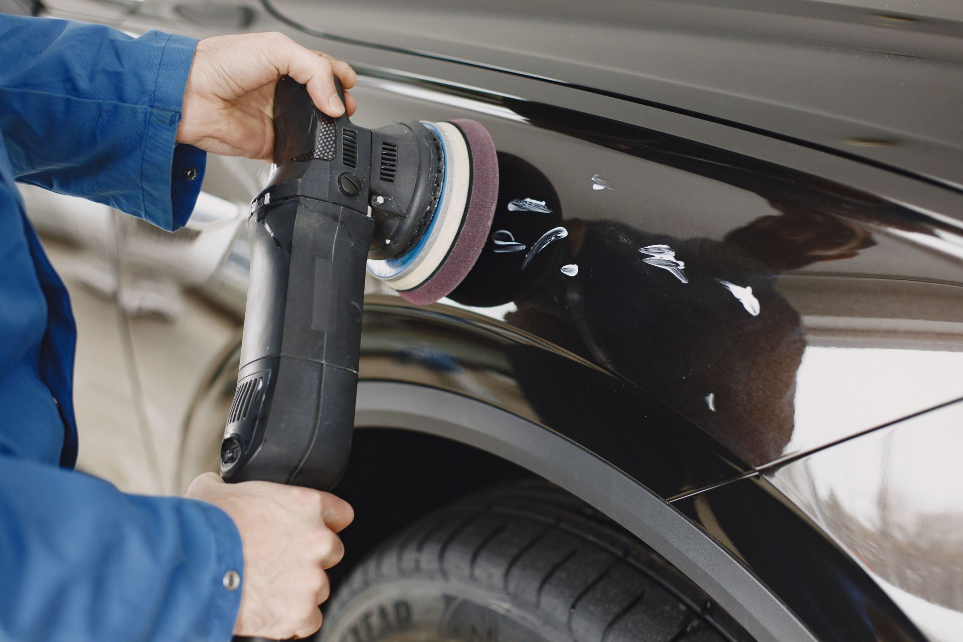 Hands using a polishing machine on a car's surface in a garage setting.